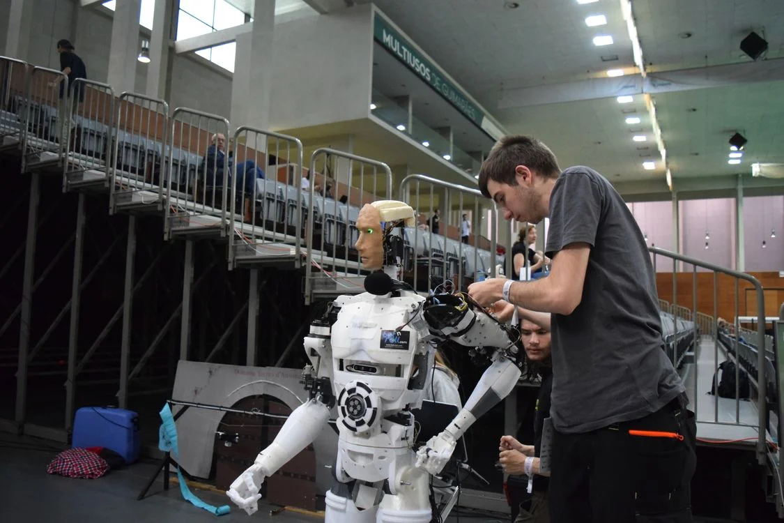 A technician assembling a humanoid robot at a technology exhibition, representing the setup work behind AI for agency operations