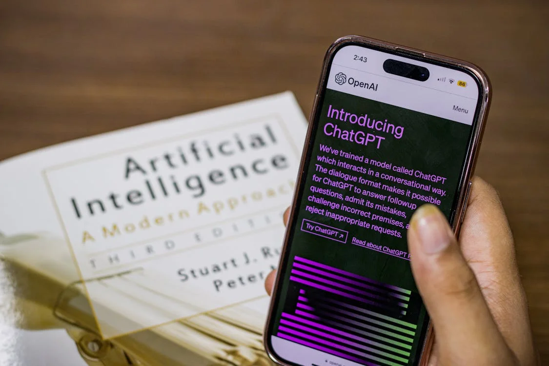 ChatGPT app on a smartphone over an open AI textbook — the information tools that cannot replace contextual expertise