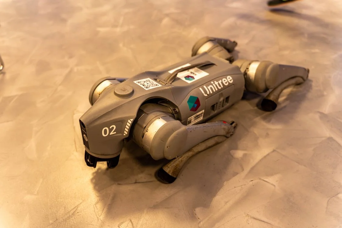 A Unitree robot dog resting on a concrete floor, representing a system that carries your methodology to every client so you are not the one delivering it