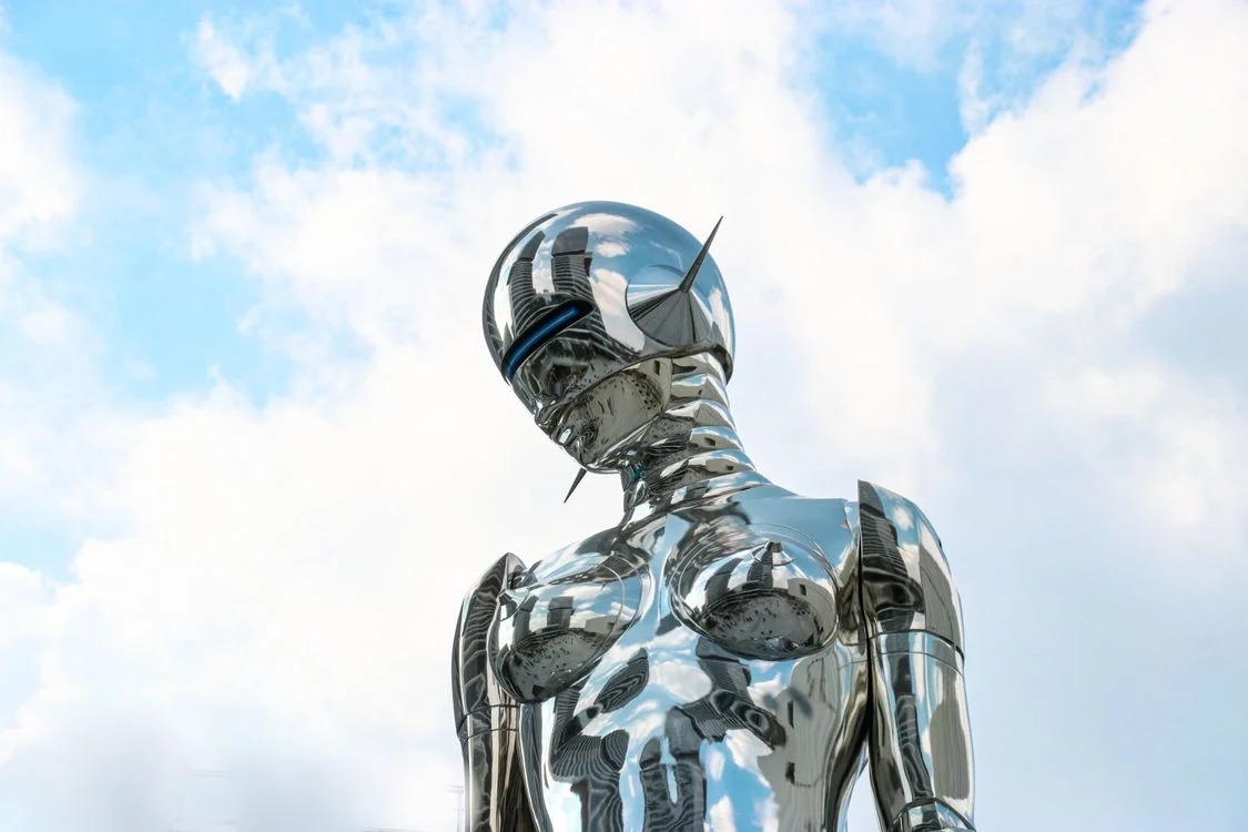 A polished chrome robot sculpture against a bright blue sky, representing AI for agency operations running the machinery behind client delivery