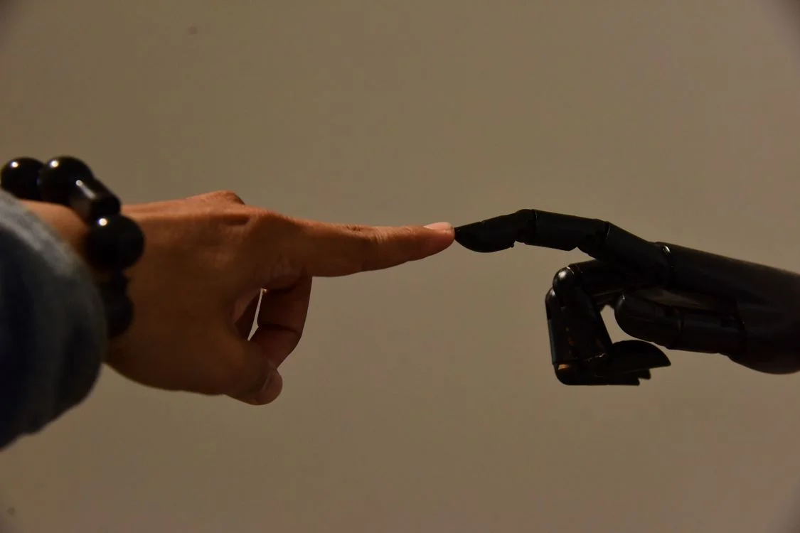 A human finger and a robotic finger meeting at a single point, representing your methodology reaching each client inside their own isolated AI workspace