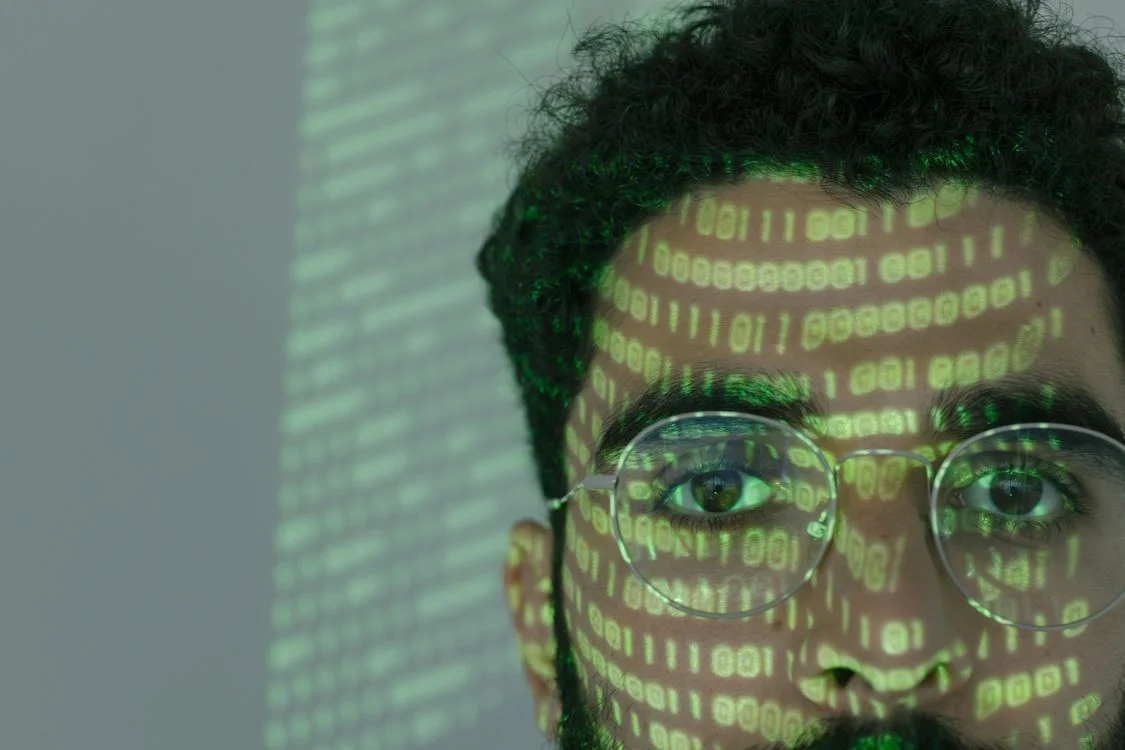 Close-up of a person with green binary code projected across their face, representing the client context an agency carries in people's heads instead of in a system