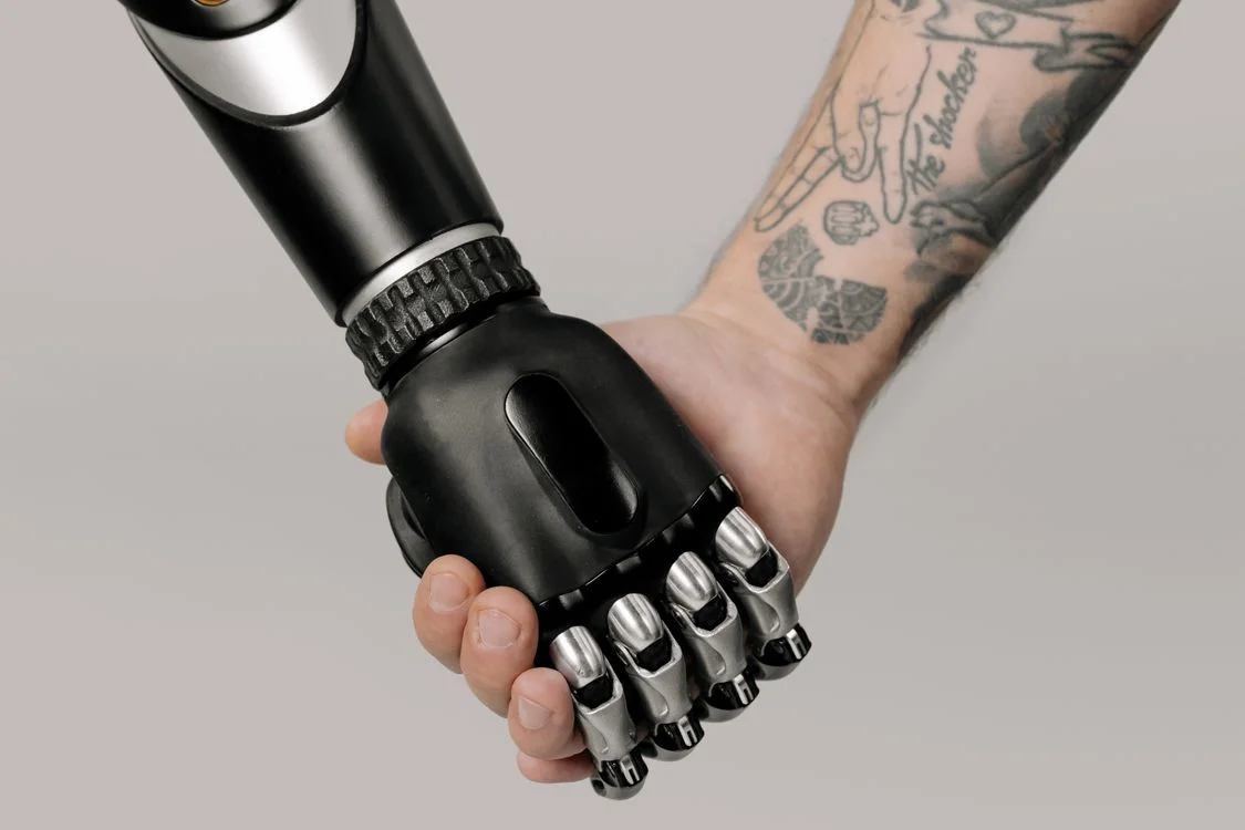 A robotic hand and a human hand clasped together, representing the future of high-ticket coaching as a split between machine delivery and human judgment