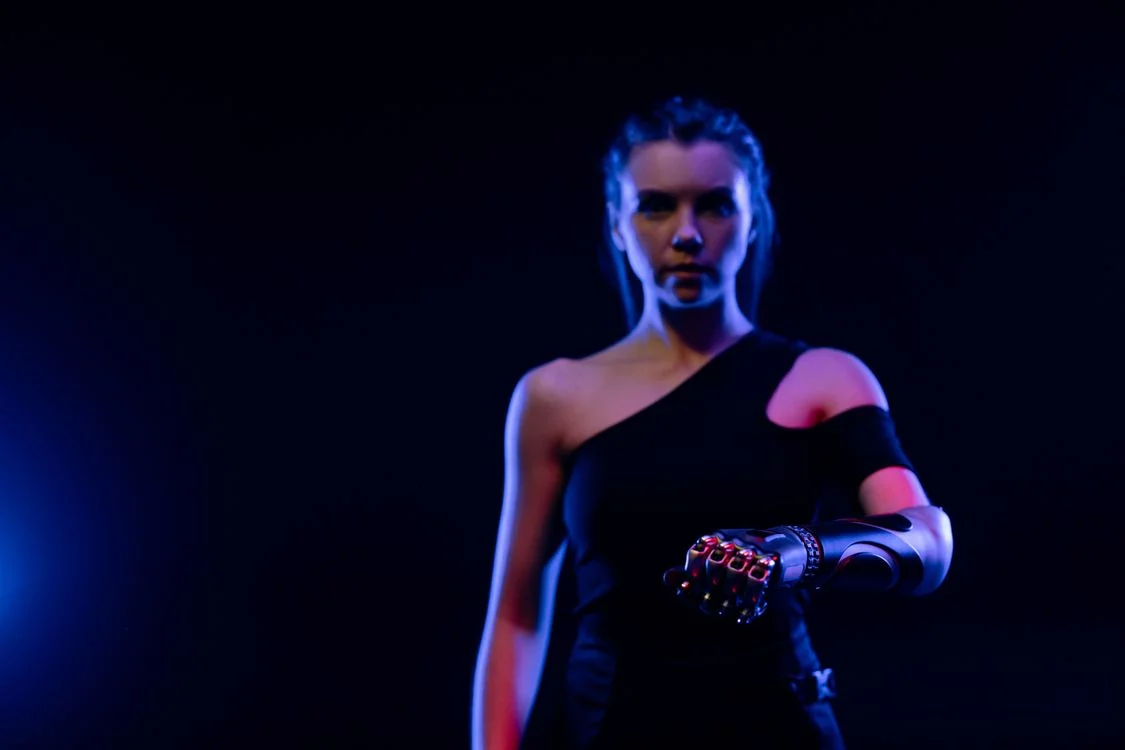 A woman with a cybernetic arm lit in blue and red, representing the future of high-ticket coaching where the machine half carries delivery and the human half carries judgment