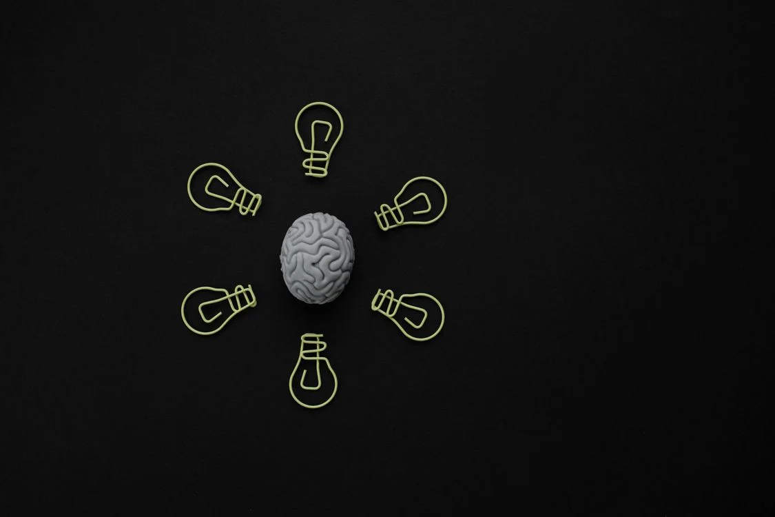 A model brain surrounded by light-bulb shaped paper clips on a black background, representing the judgment of deciding when ChatGPT is safe for client work