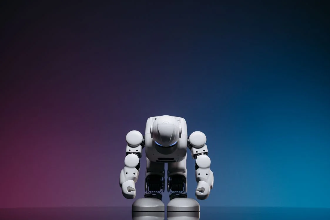 A white humanoid robot bowing on a gradient background, representing a system that carries your methodology so you stop re-supplying it for every client