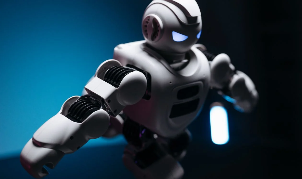 White toy robot with glowing eyes on a blue and pink backdrop, representing the AI system that will hold your captured methodology