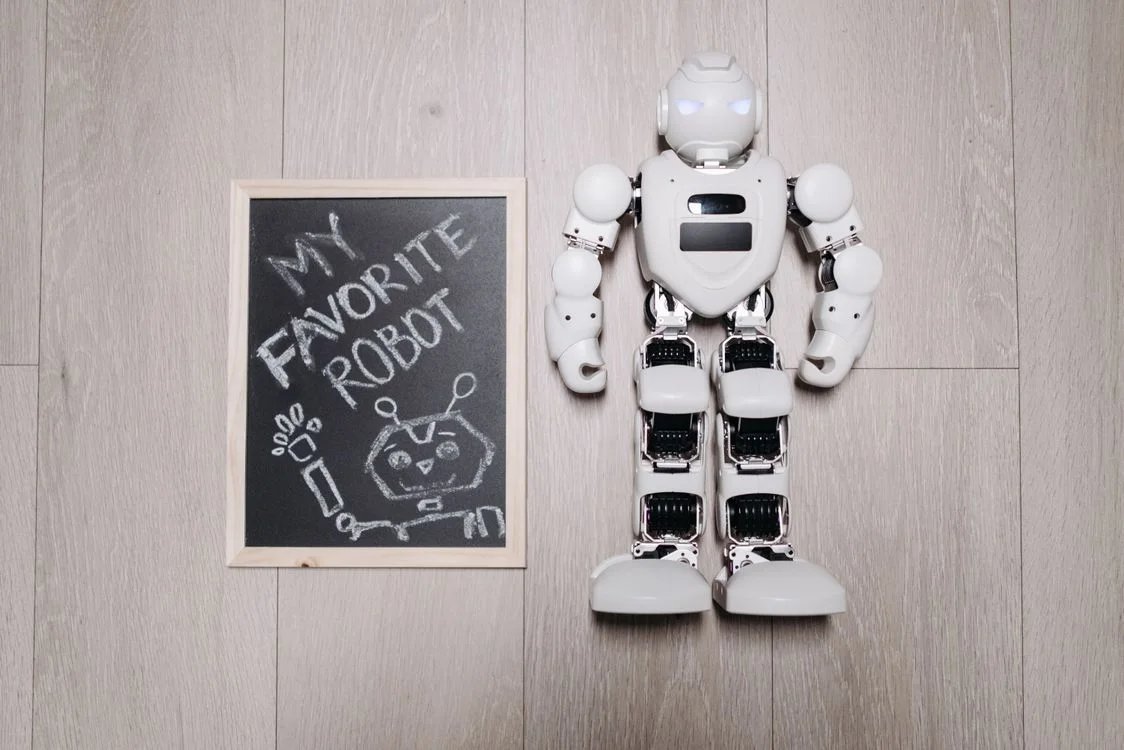 A white robot beside a chalkboard, representing AI that can now produce the packaged information once sold as an info product