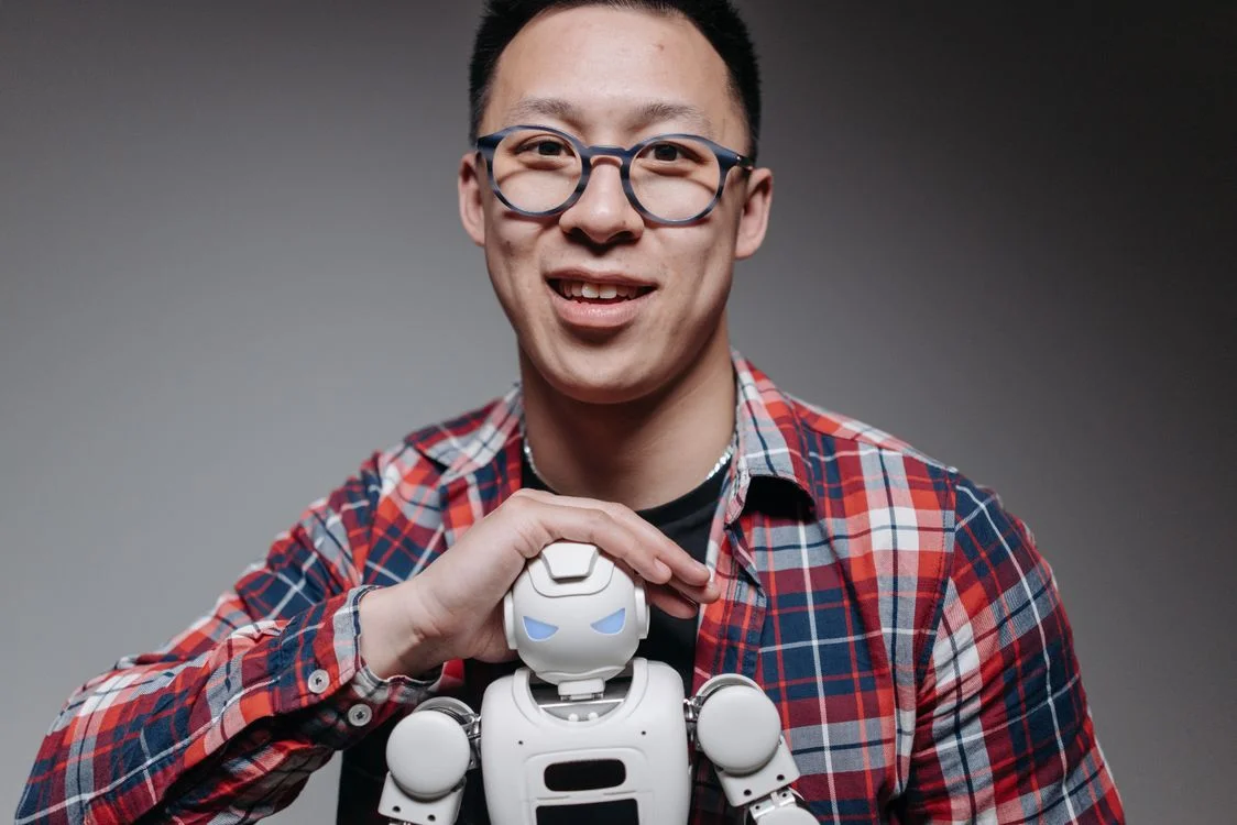 A man holding a small robot in a studio, representing an operator choosing a business model that works with AI rather than competing against it