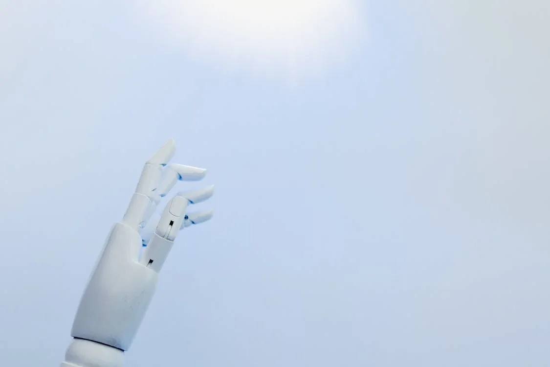 A robotic hand reaching toward a bright light, representing AI for coaches that extends a coach's methodology without replacing the coach