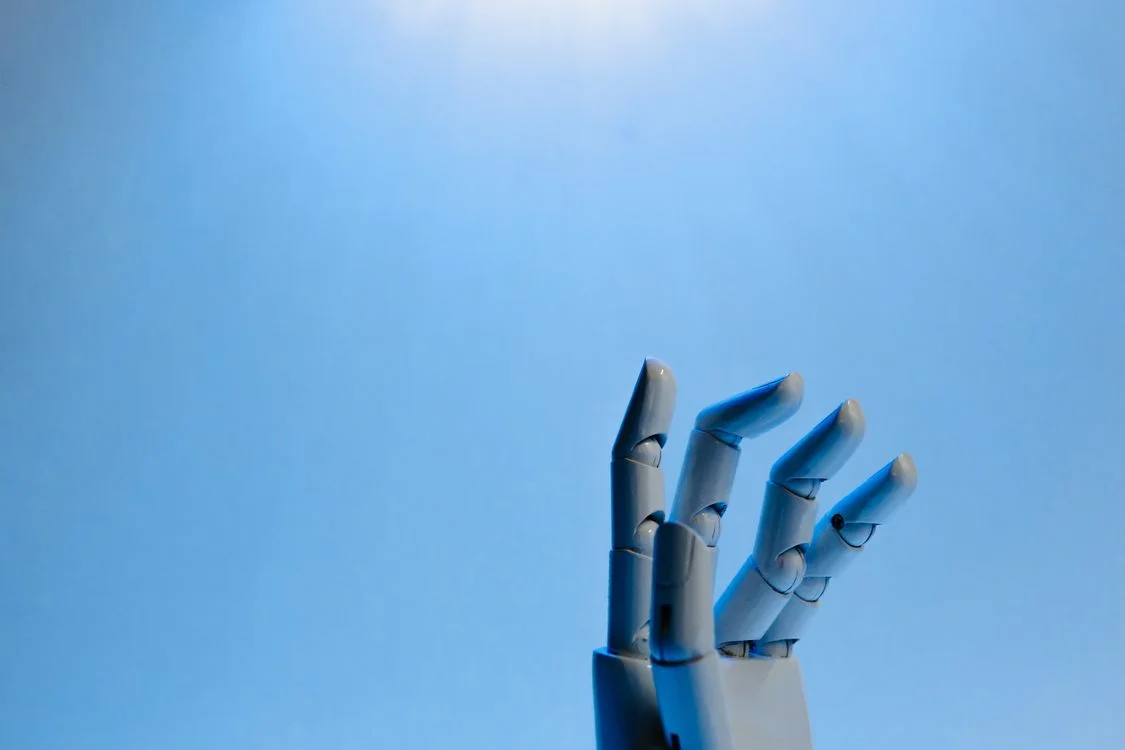 White robotic hand reaching upward toward light against a blue sky, representing the question of whether Microsoft Copilot is safe for confidential client work