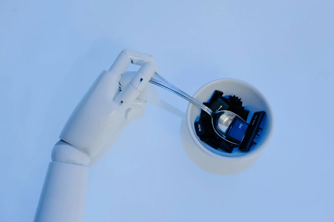 A robotic hand holding a spoon of keyboard keys, representing a system that carries your methodology to every client instead of you delivering it by hand