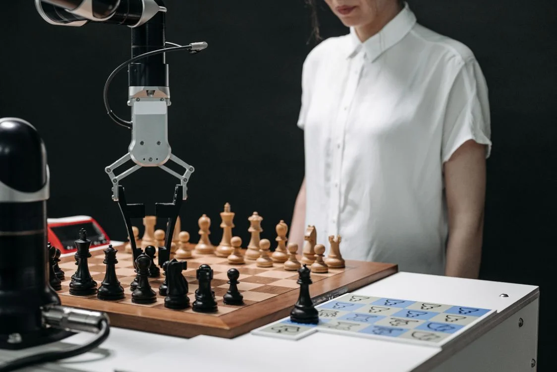Robotic arm and a person playing chess, representing the consultant directing the AI client onboarding process rather than producing every plan by hand