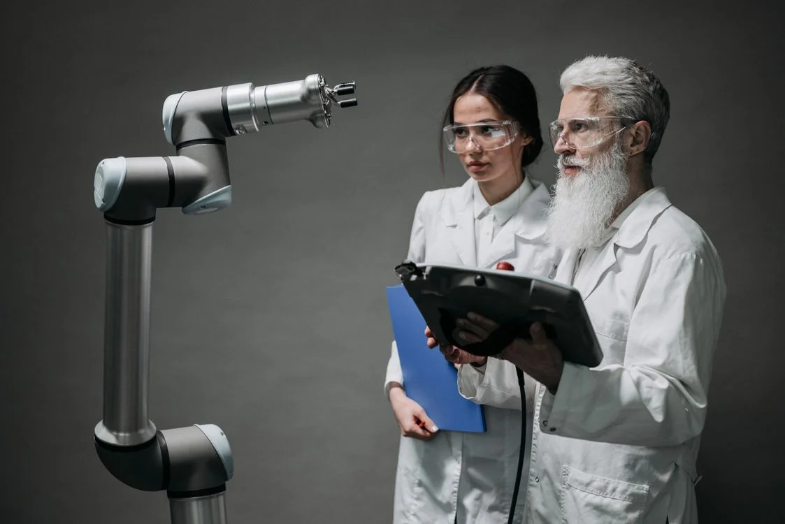 Two researchers directing a robotic arm rather than operating it by hand, the shift required to deliver your methodology to 100 clients
