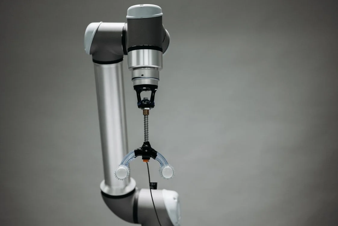 Silver industrial robotic arm with a gripper reaching down against a grey background, representing Microsoft Copilot reaching across everything in your tenant rather than isolating each client