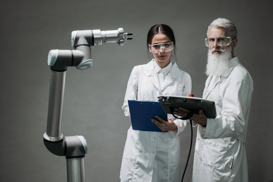 Two scientists in white lab coats reviewing a clipboard beside a grey robotic arm, representing the accountability and audit trail that safe AI for client work requires