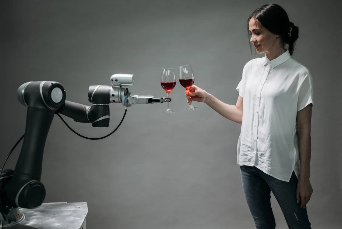 A person raising a glass with a robotic arm, representing a direct response marketing consultant working alongside an AI system rather than being replaced by it