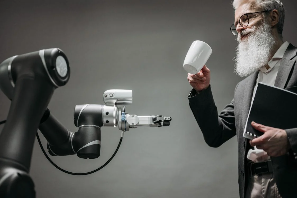 A robotic arm handing a coffee cup to a bearded man in a suit, representing an AI agent taking the routine work off a consultant
