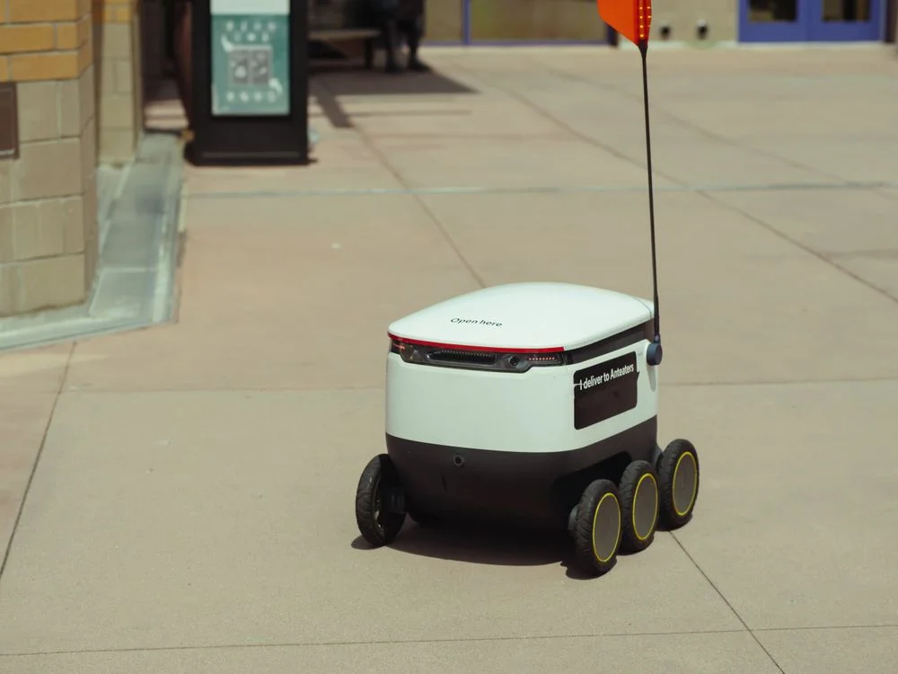An autonomous delivery robot moving along a city sidewalk, representing the business models that work with AI rather than compete with it