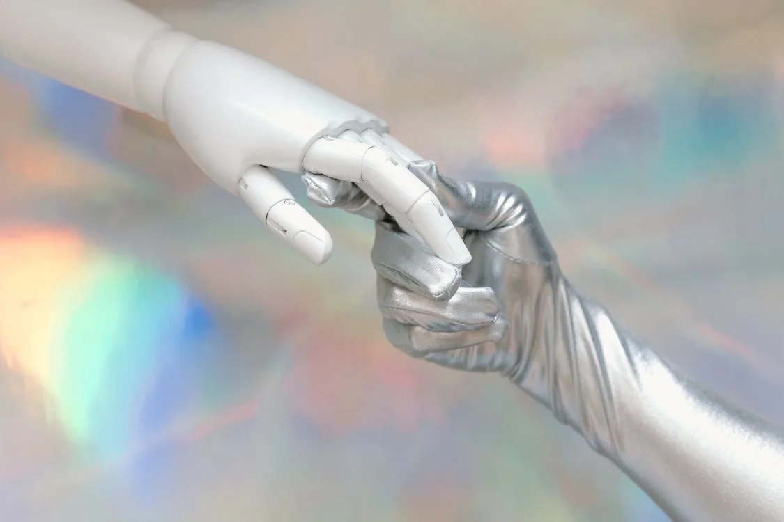 A robotic hand and a human hand reaching toward each other, representing the partnership between a practitioner and an AI system that lets them serve more clients without burning out