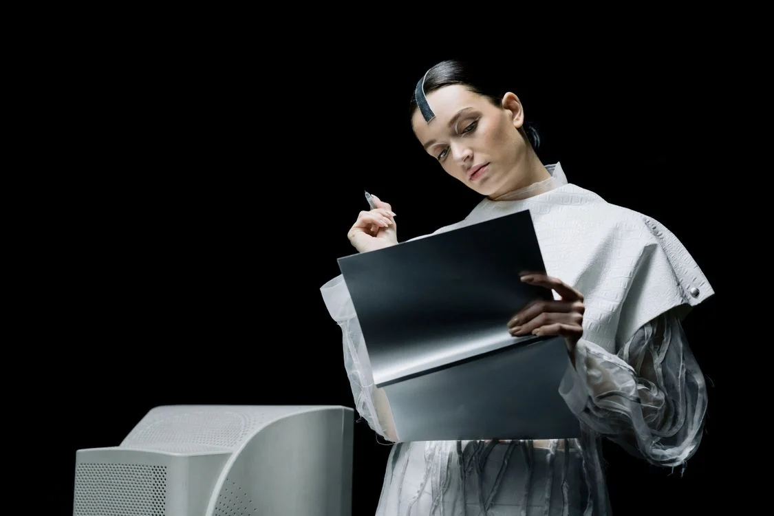 A figure in futuristic white attire reviewing a document beside a machine, representing generic AI reading client material with no idea which client it belongs to
