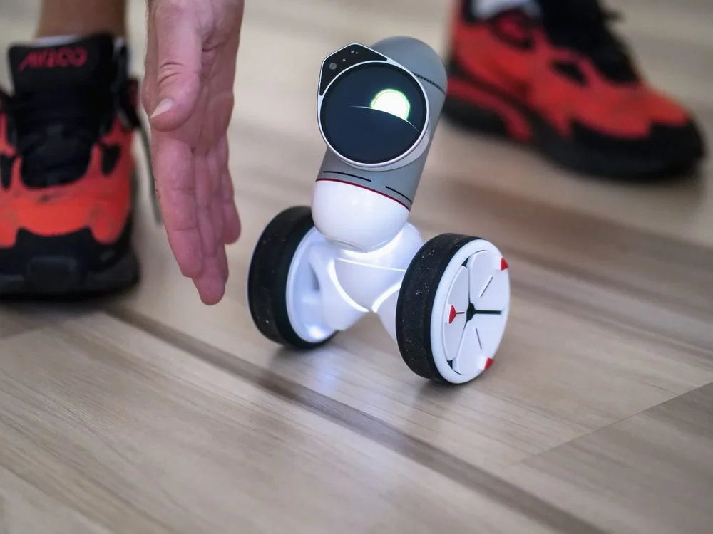 A hand guiding a small autonomous robot, showing the coach directing the system rather than delivering every session